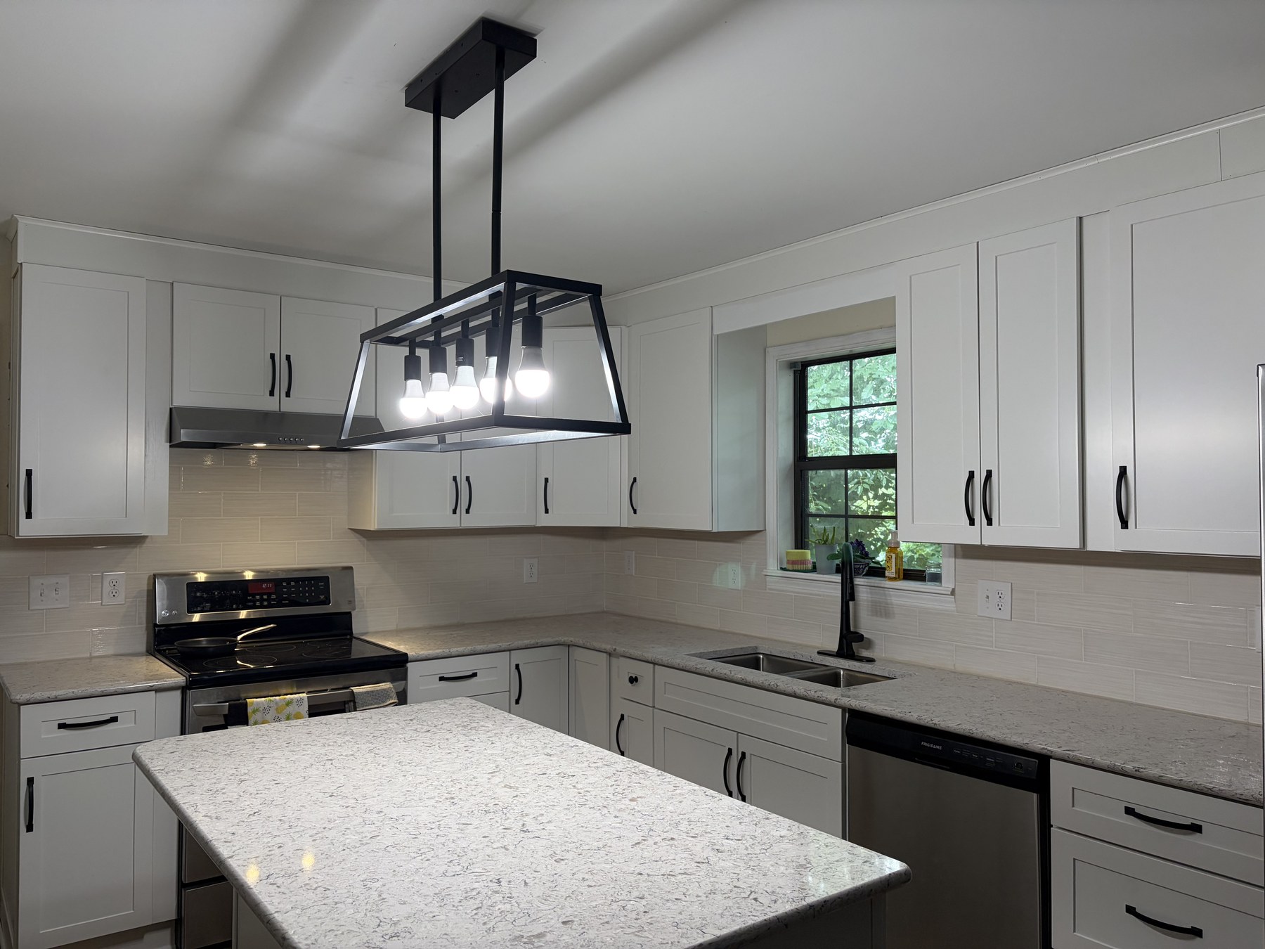 Finished white shaker kitchen with subway-tile backsplash, speckled granite island, black fixtures, and a linear pendant light