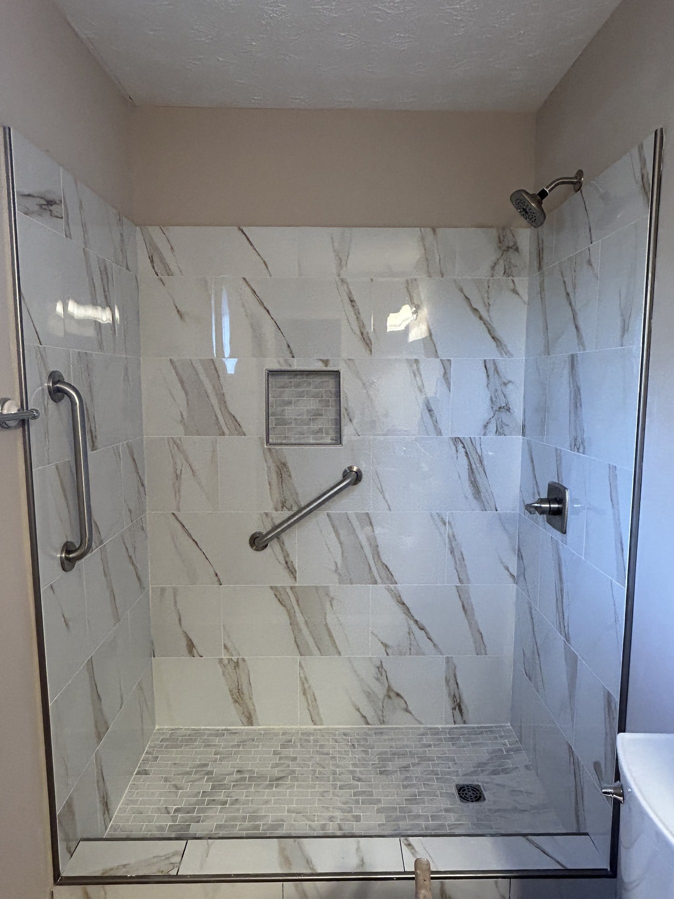 Finished walk-in shower with Calacatta-style tile, recessed niche, and pebble mosaic floor