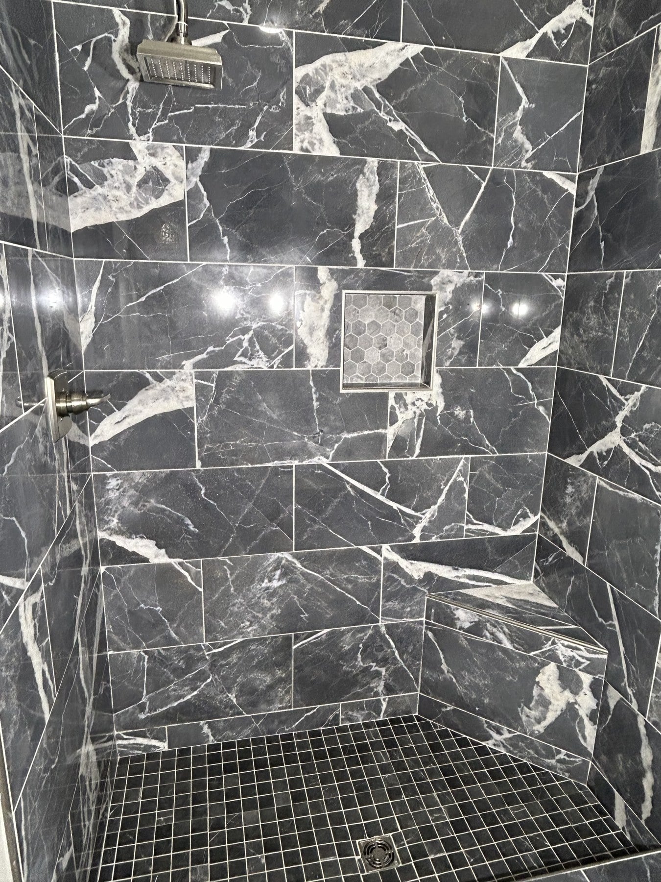 Finished walk-in shower with dramatic dark tile, hexagonal mosaic niche, and black mosaic floor