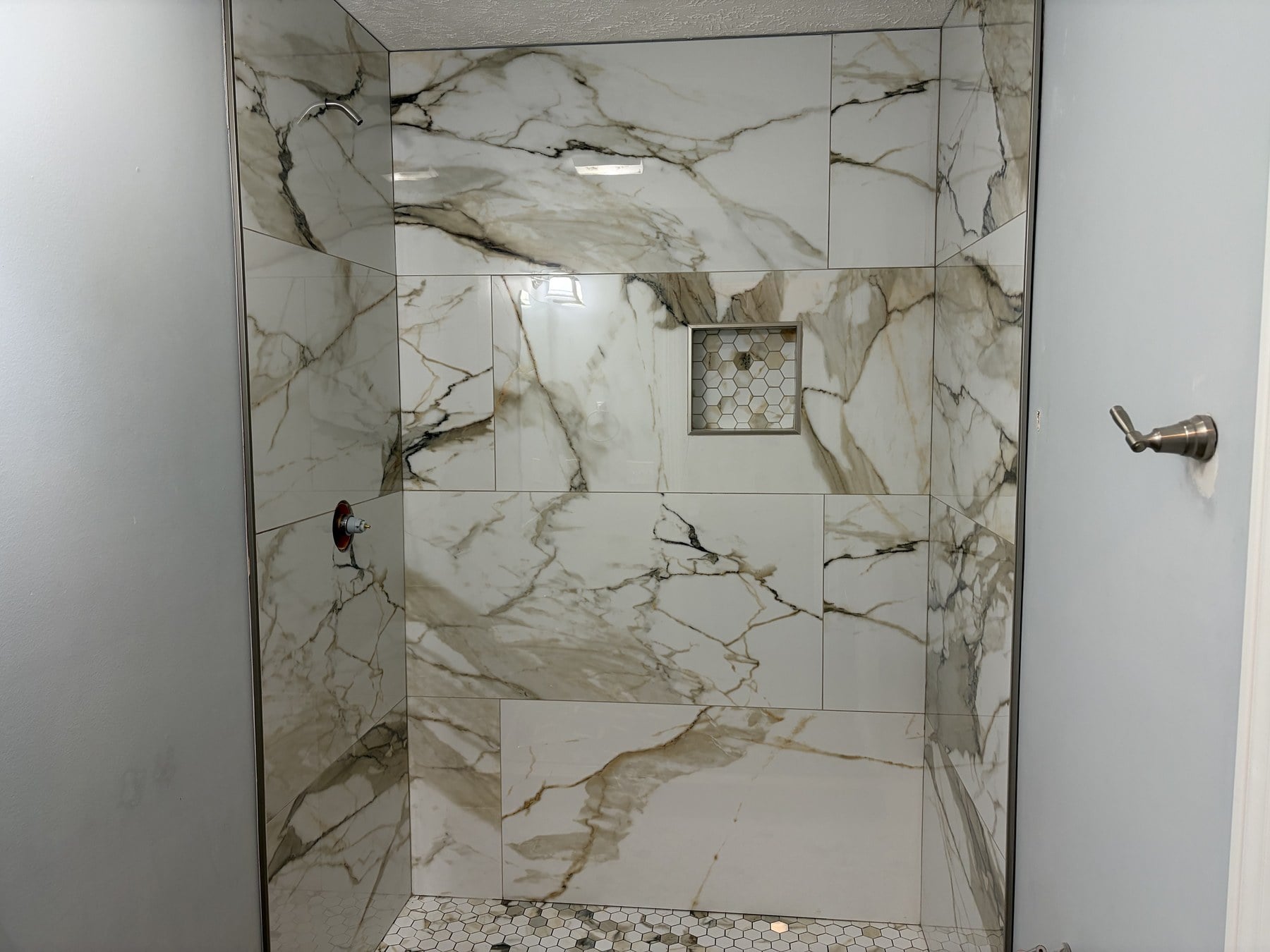 Finished walk-in shower with gold-veined Calacatta-style tile, hex niche, and penny-round floor
