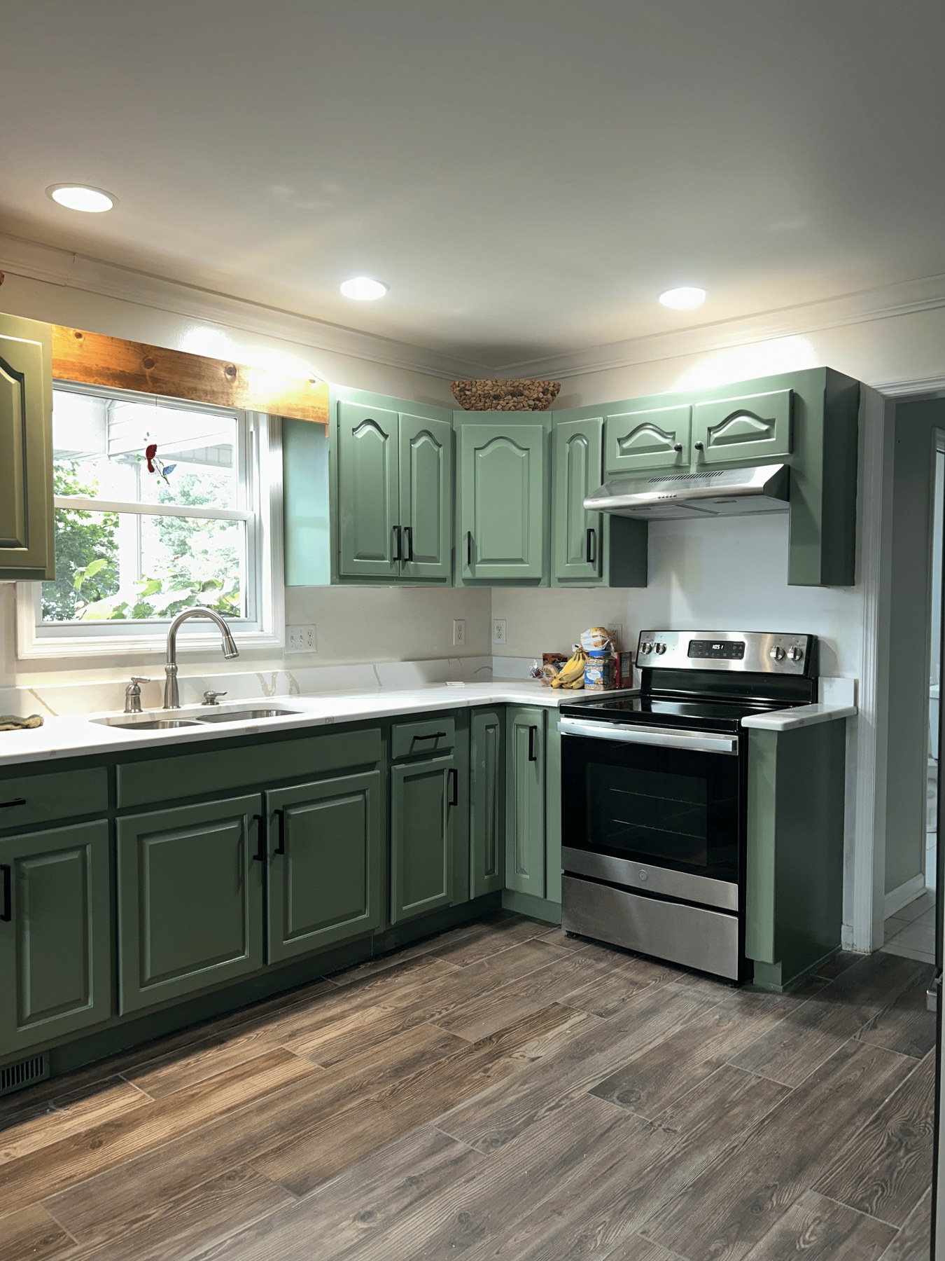 Finished kitchen with sage-green cabinets, white quartz counters, and wood-look tile floor