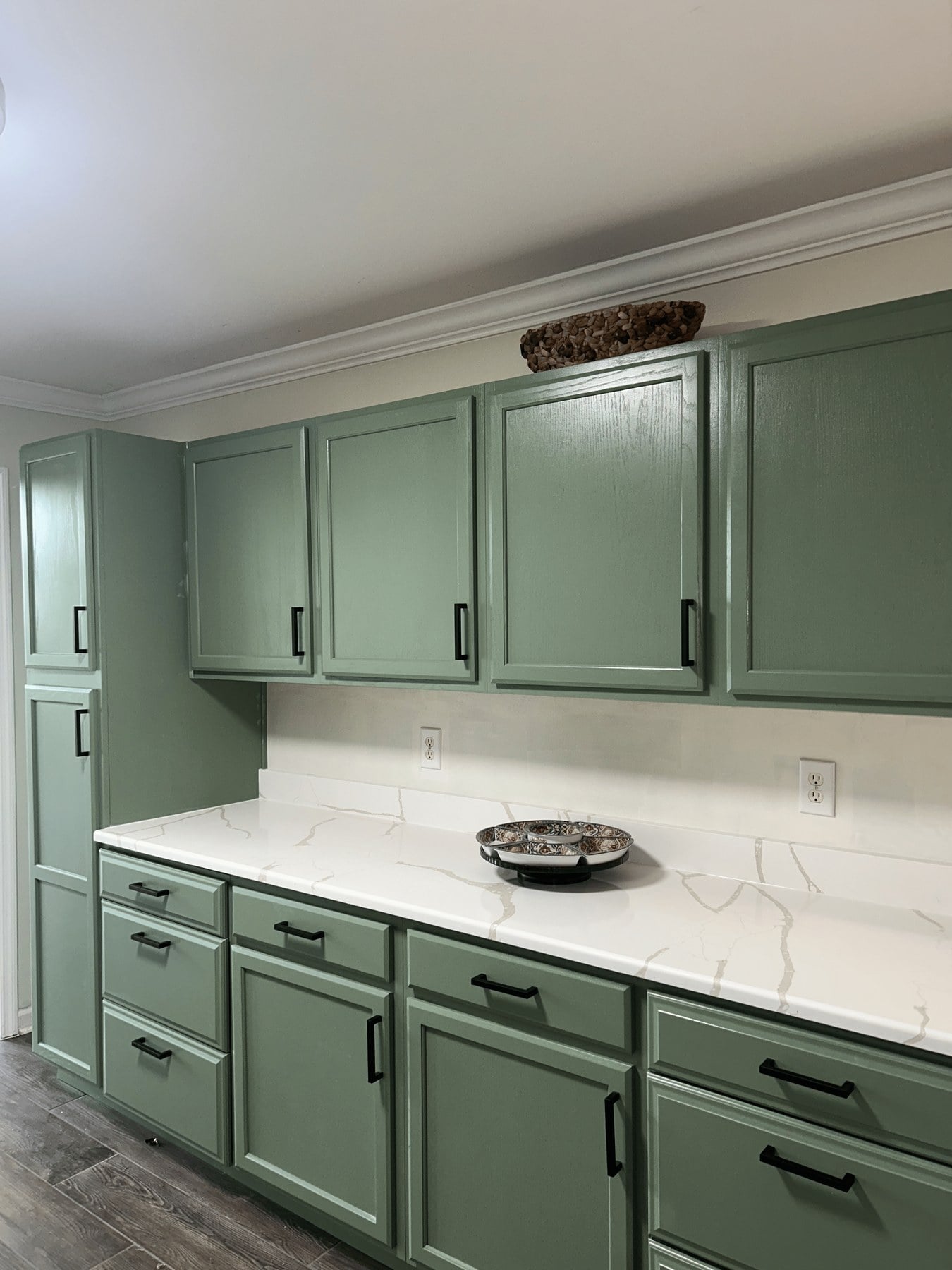 Sage-green cabinets with white quartz countertops, quartz backsplash, and black hardware