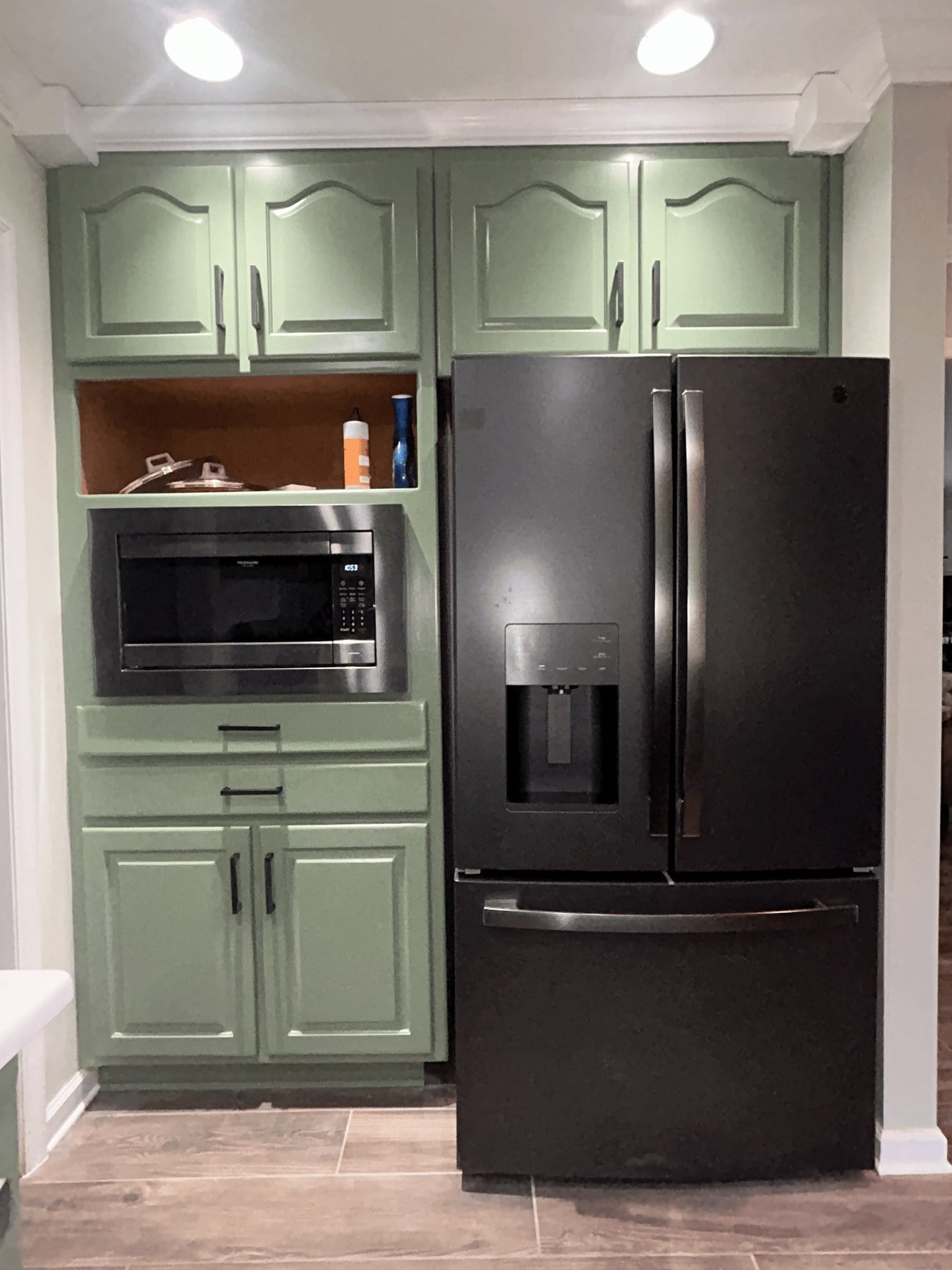 Sage-green pantry cabinetry with black-stainless French-door refrigerator and built-in microwave