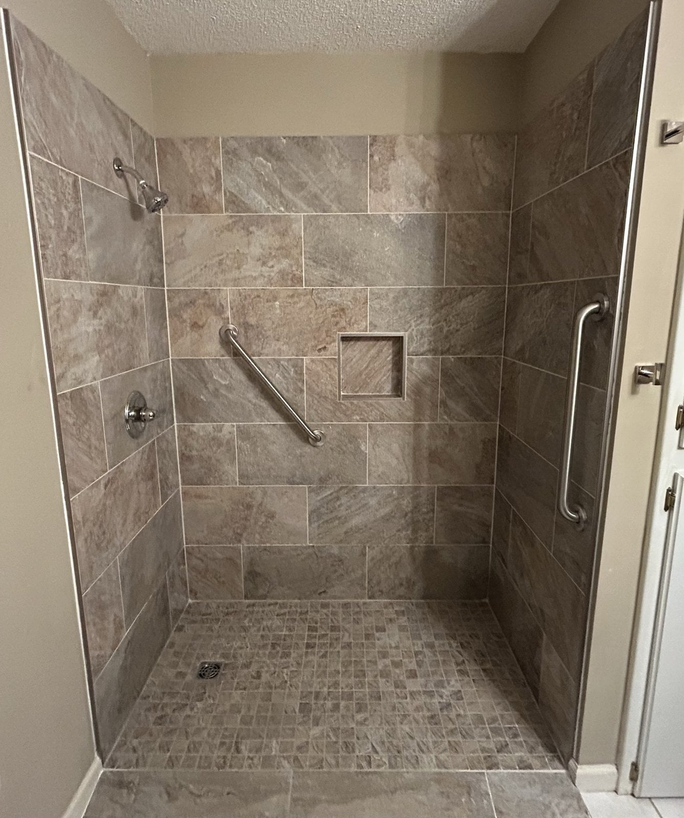 Finished accessible walk-in tile shower with grab bars, recessed niche, and mosaic floor