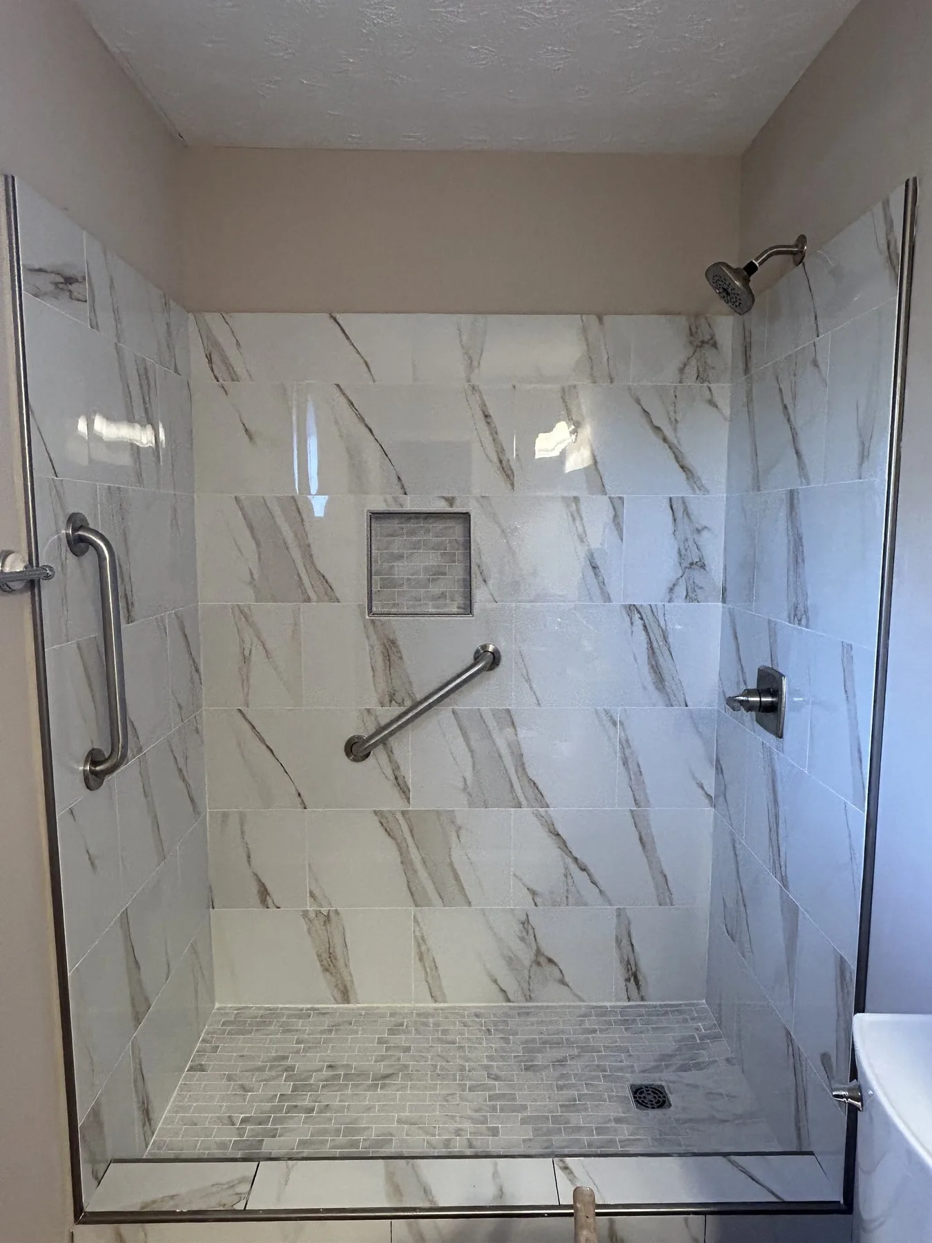 Finished walk-in shower with Calacatta-style tile, recessed niche, and pebble mosaic floor