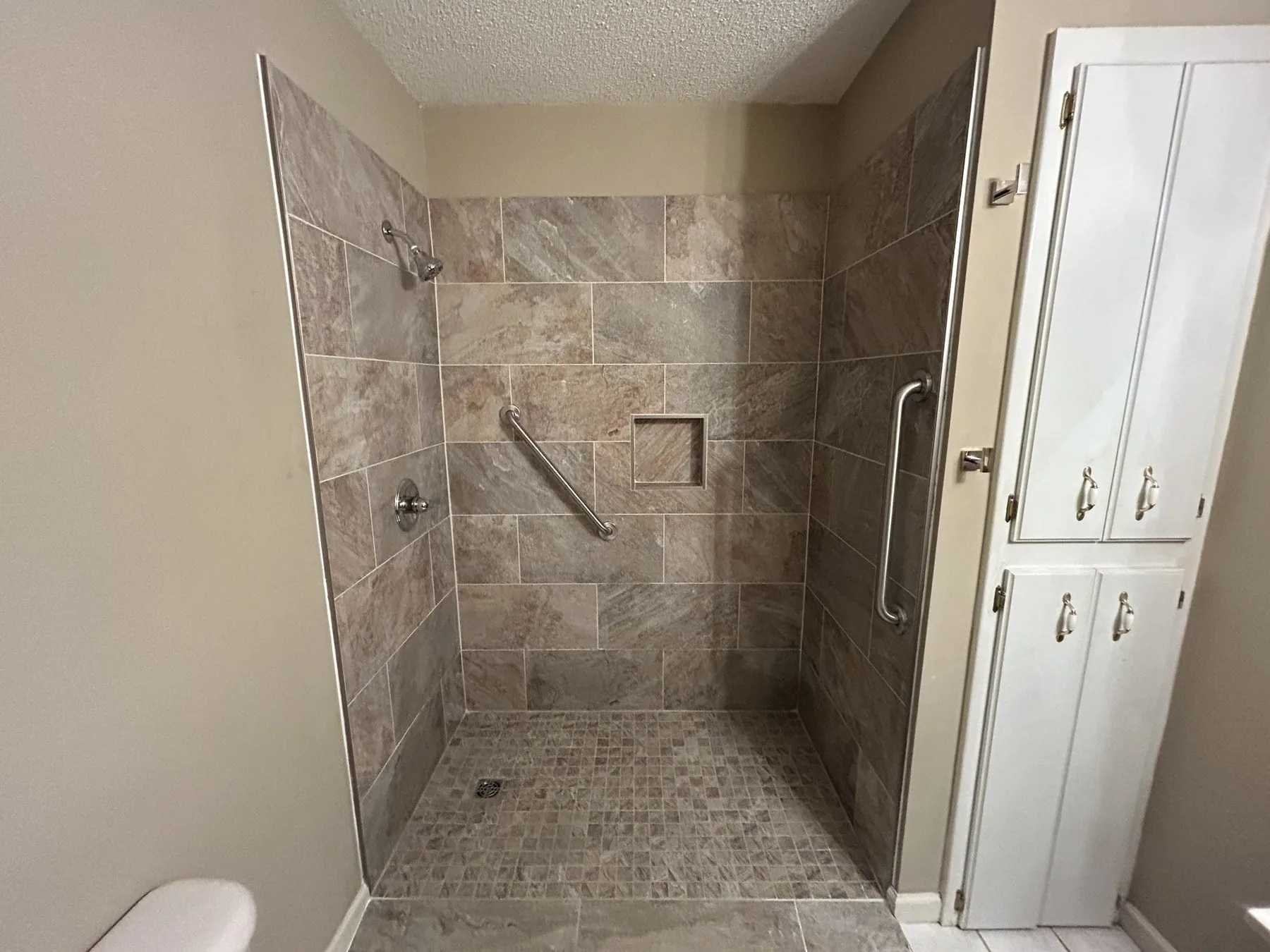 Finished travertine walk-in shower with grab bars, recessed niche, and pebble mosaic floor