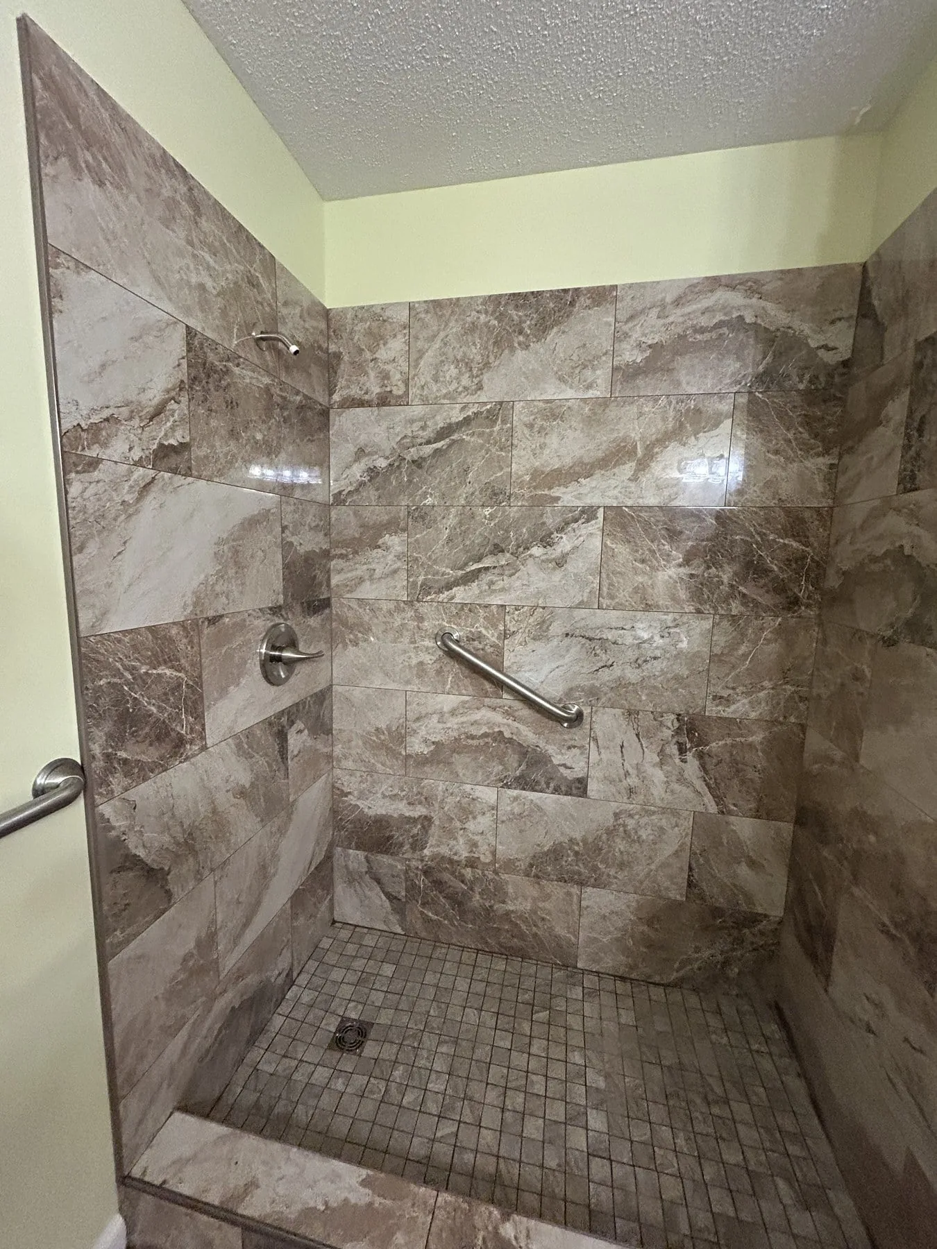 Finished light-brown tile walk-in shower with grab bar and small-format floor mosaic