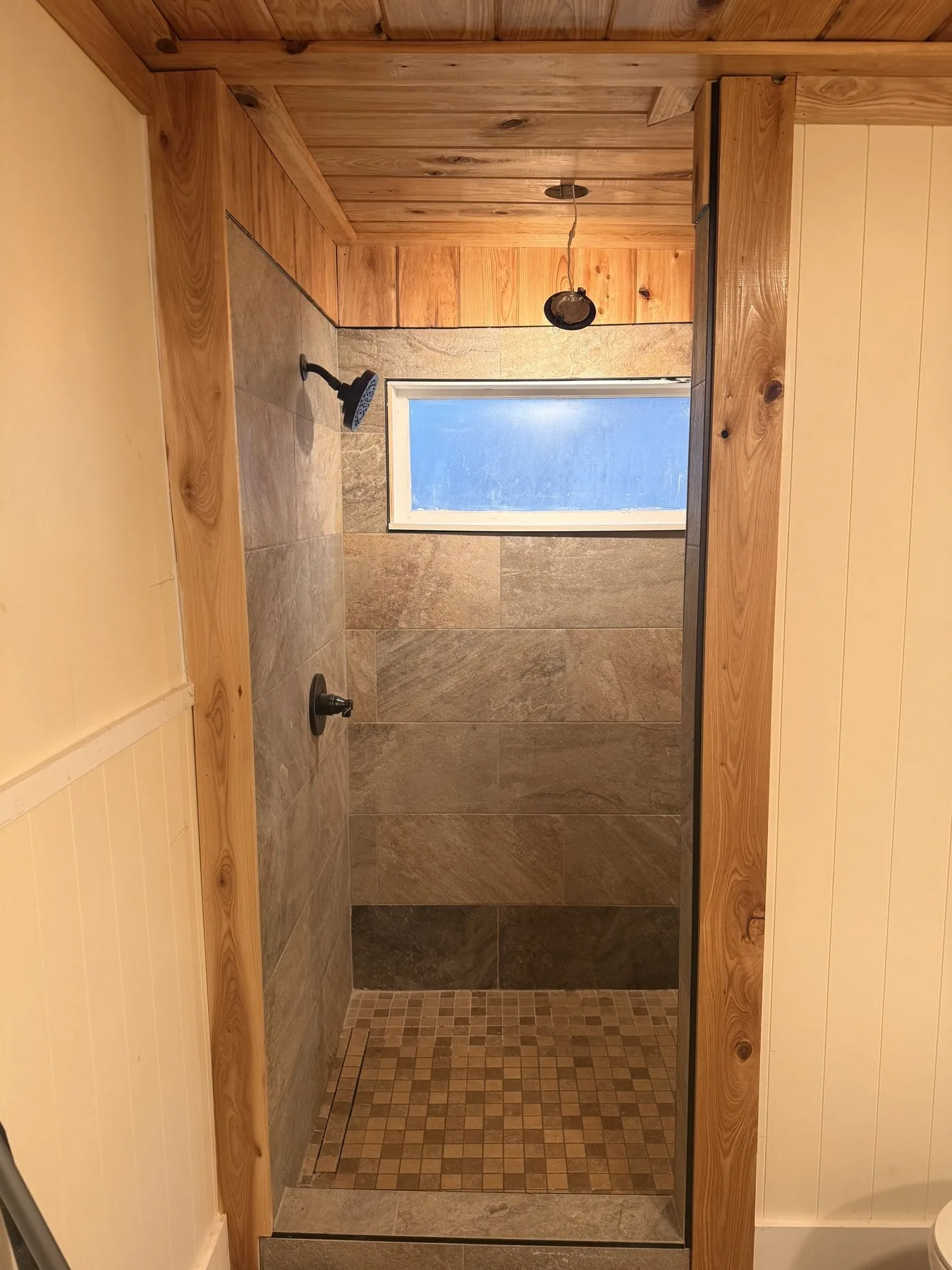 Finished walk-in shower with cedar-plank ceiling, slate-look tile walls, and pebble mosaic floor