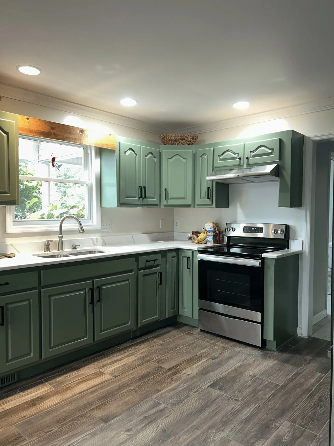 Finished kitchen with sage-green cabinets, white quartz counters, and wood-look tile floor