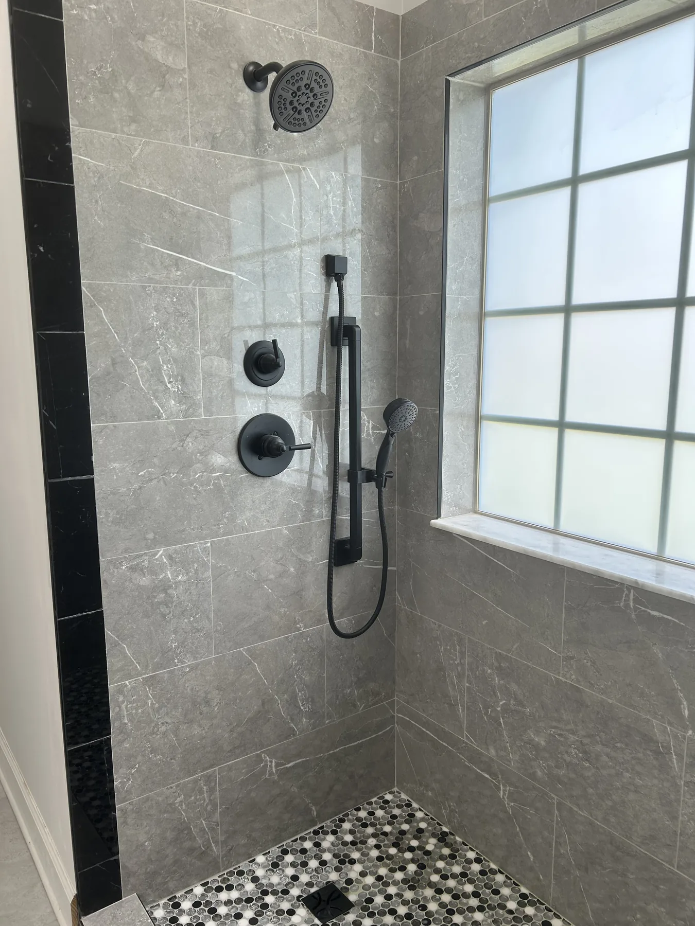 Matte black rain head, handheld slide bar and valves set into grey marble-look tile