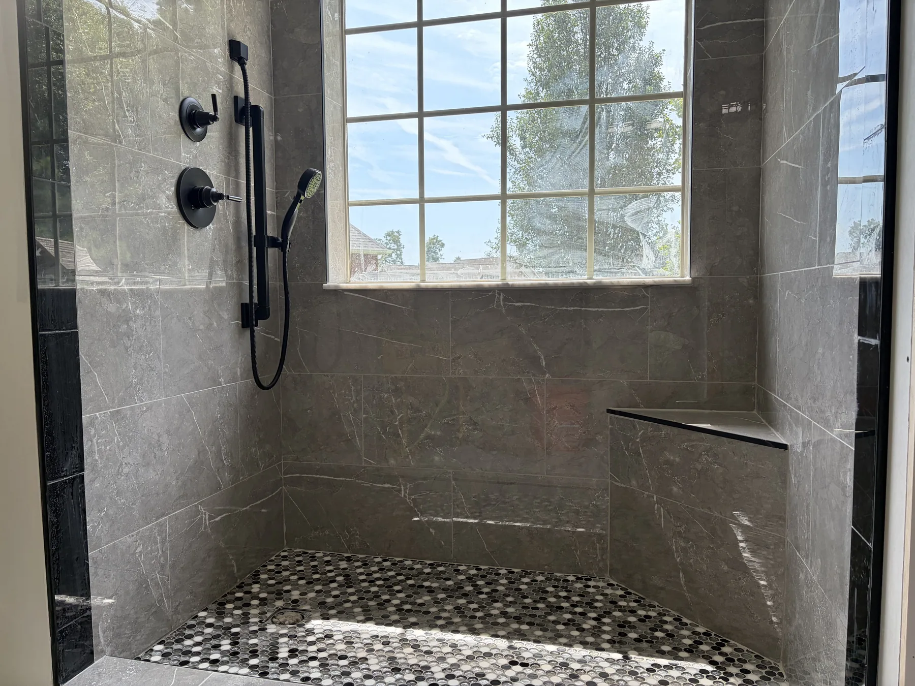 Walk-in shower with black edge trim, tiled bench and black and white mosaic floor