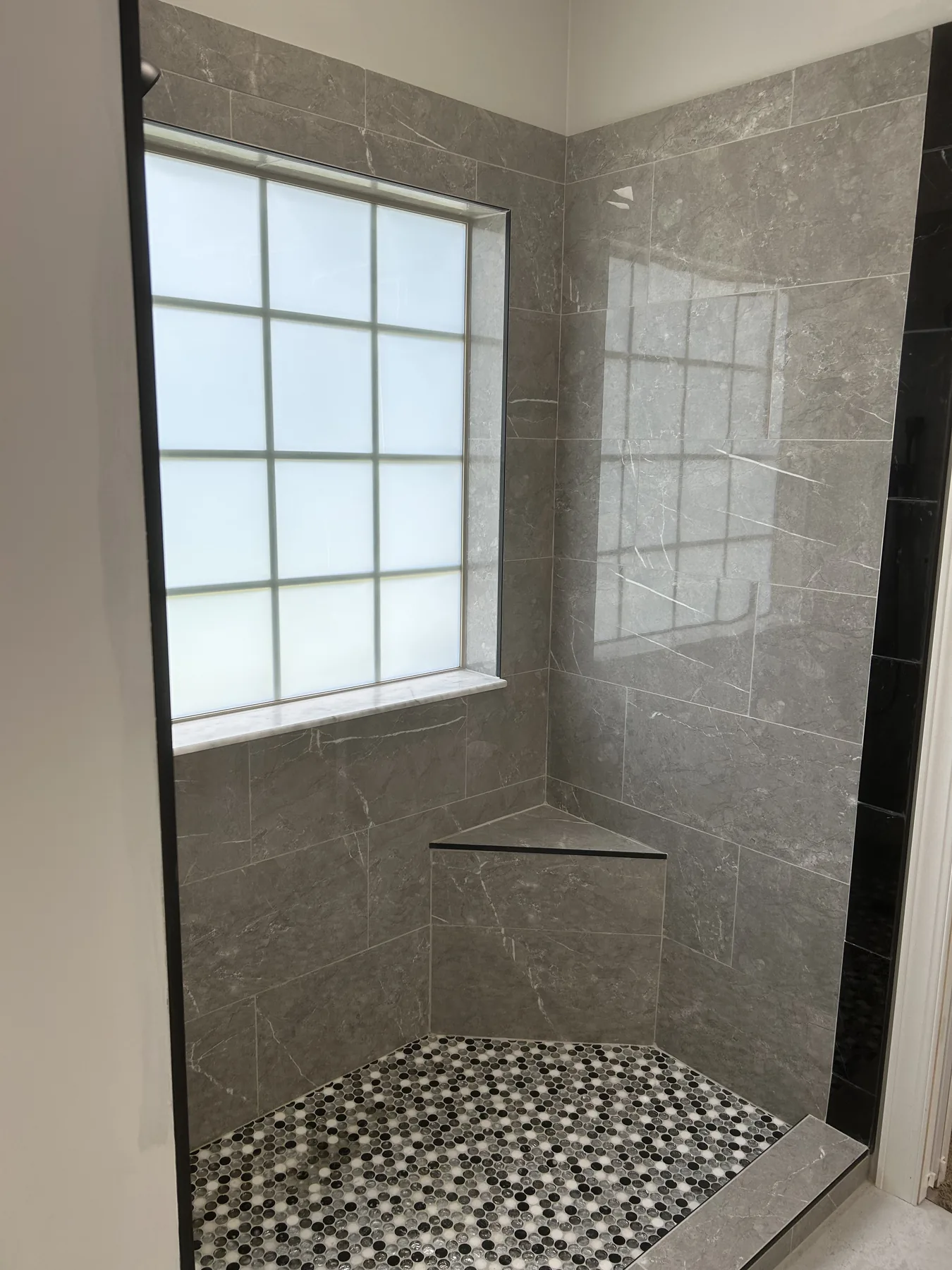 Grey marble-look tile shower mid-build with corner bench and penny mosaic floor set