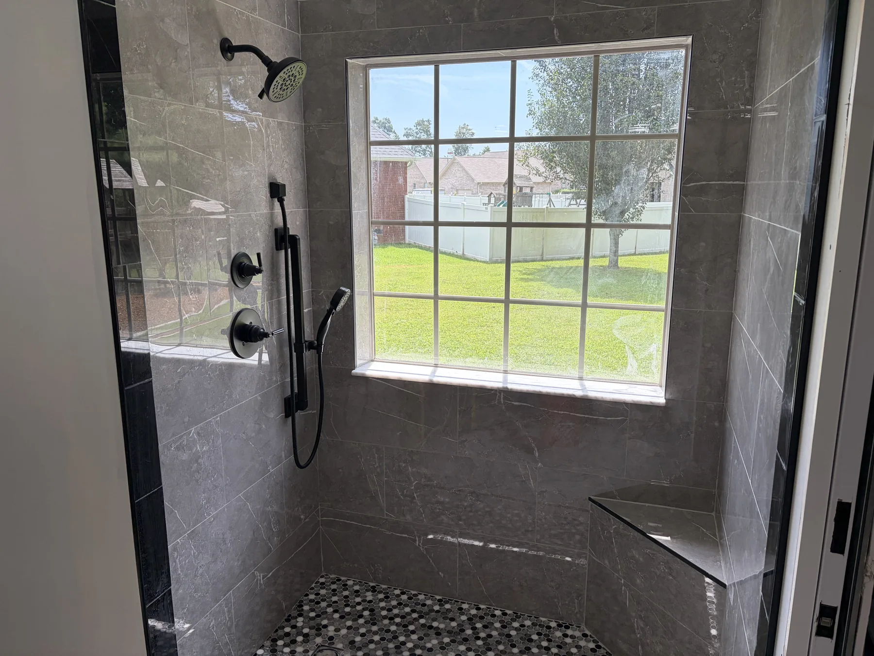 Walk-in shower with black fixtures, interior window and black tile accent band