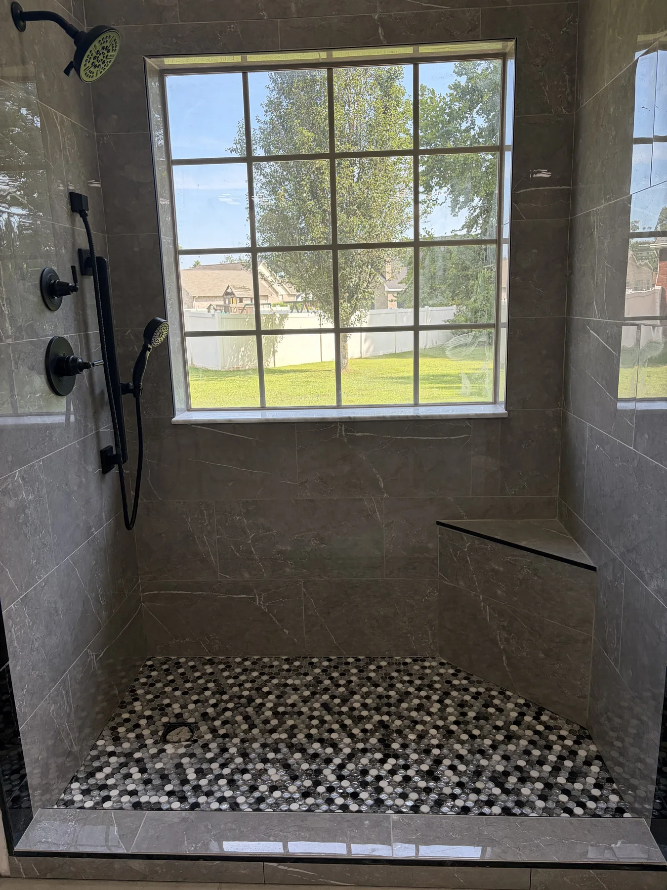 Walk-in shower floor in black and white penny round mosaic with a tiled corner bench